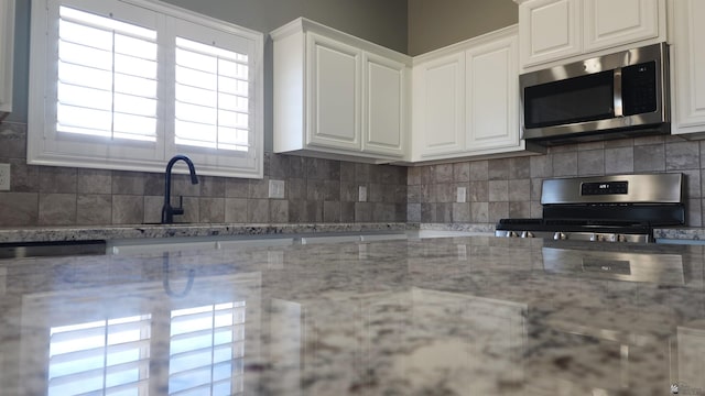kitchen featuring decorative backsplash, white cabinetry, appliances with stainless steel finishes, and light stone countertops