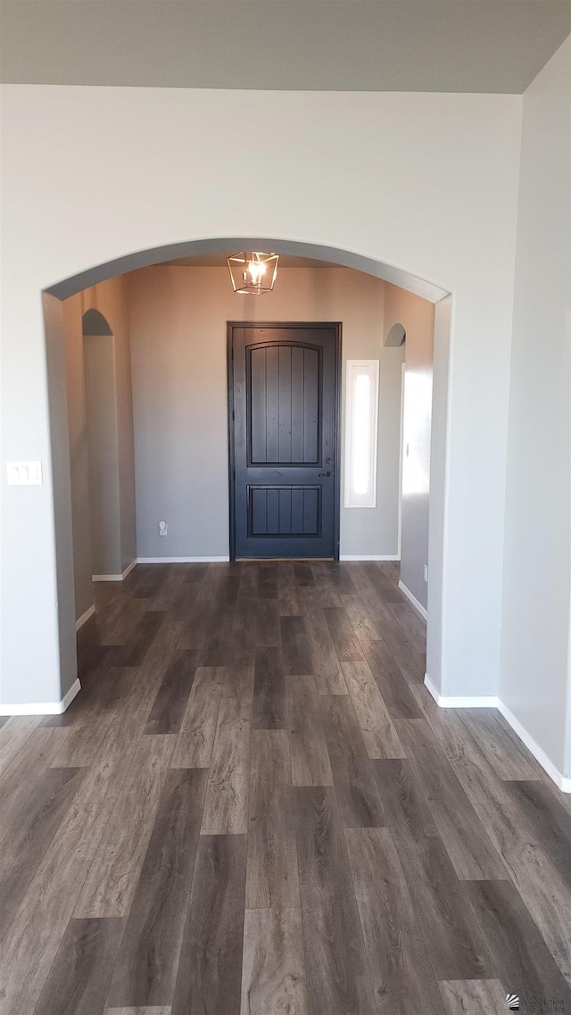 entrance foyer with arched walkways, baseboards, and dark wood-type flooring