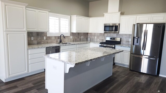 kitchen featuring dark wood-style flooring, a kitchen island, tasteful backsplash, a sink, and appliances with stainless steel finishes