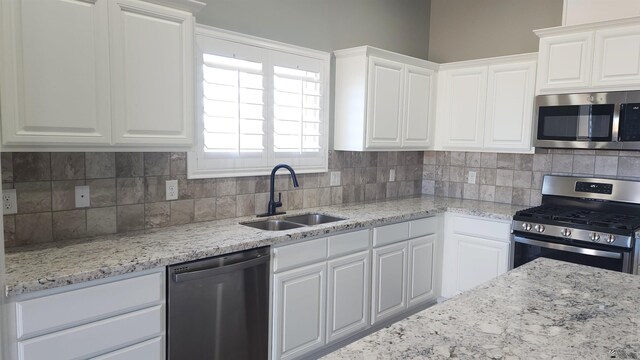 kitchen featuring white cabinets, tasteful backsplash, light stone counters, a sink, and appliances with stainless steel finishes