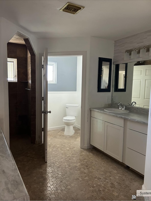 bathroom featuring visible vents, brick floor, toilet, and vanity