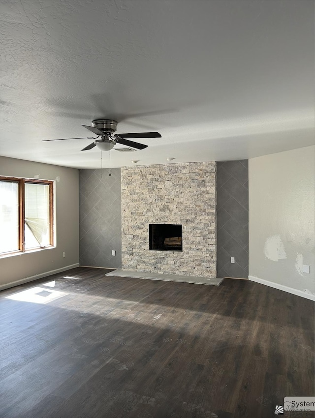 unfurnished living room with baseboards, a ceiling fan, a stone fireplace, and dark wood-type flooring