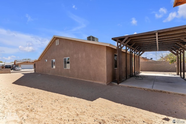 view of side of property featuring stucco siding, a patio, central AC, and fence