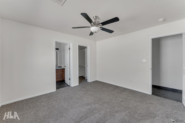 unfurnished bedroom featuring a spacious closet, baseboards, dark colored carpet, and connected bathroom