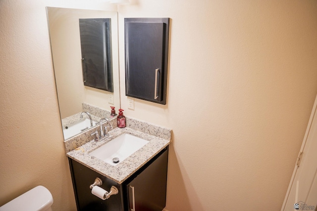 half bathroom featuring toilet, a textured wall, and vanity