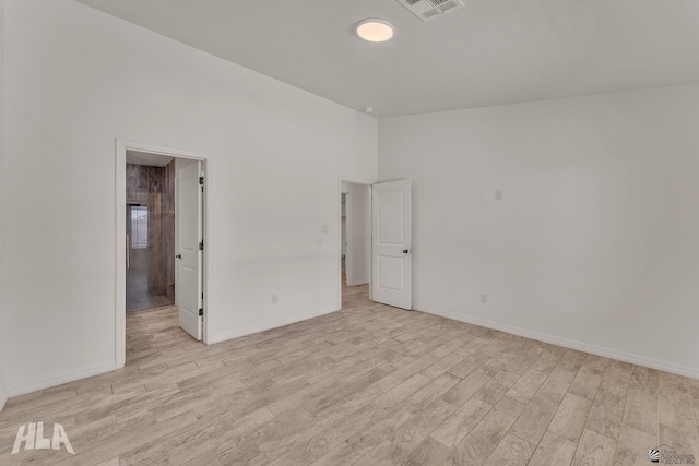 unfurnished room with lofted ceiling, light wood-style flooring, visible vents, and baseboards