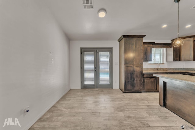 kitchen featuring light stone counters, decorative light fixtures, visible vents, a sink, and dark brown cabinetry