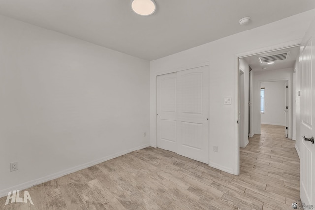 unfurnished bedroom featuring light wood-type flooring, a closet, visible vents, and baseboards