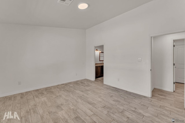 spare room featuring lofted ceiling, light wood finished floors, baseboards, and visible vents