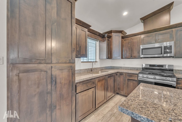 kitchen featuring light stone counters, dark brown cabinetry, a sink, appliances with stainless steel finishes, and wood tiled floor