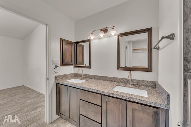 bathroom featuring double vanity, wood finished floors, a sink, and baseboards