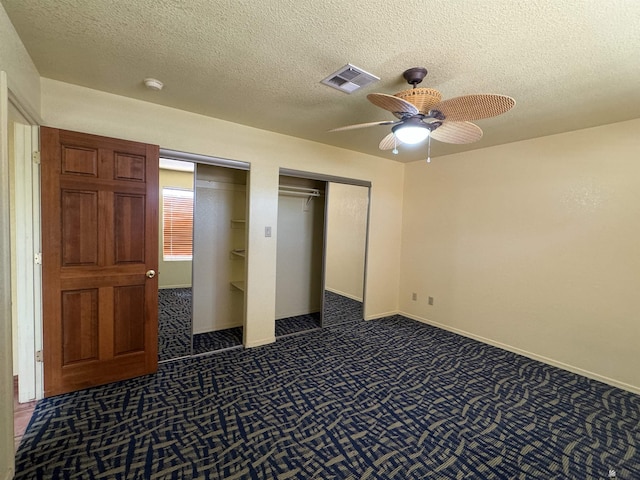 unfurnished bedroom with a ceiling fan, a textured ceiling, visible vents, multiple closets, and dark carpet