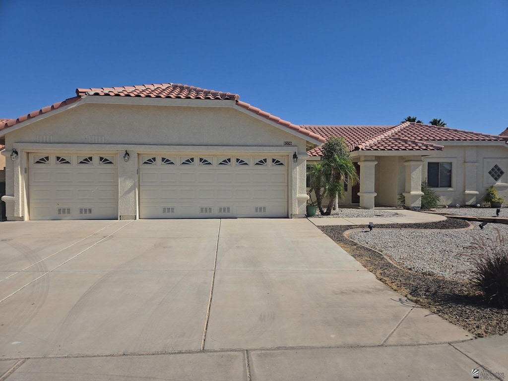 mediterranean / spanish house featuring a garage, driveway, a tile roof, and stucco siding