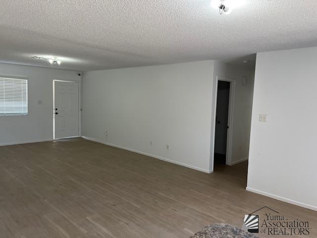 empty room with a textured ceiling, baseboards, and wood finished floors