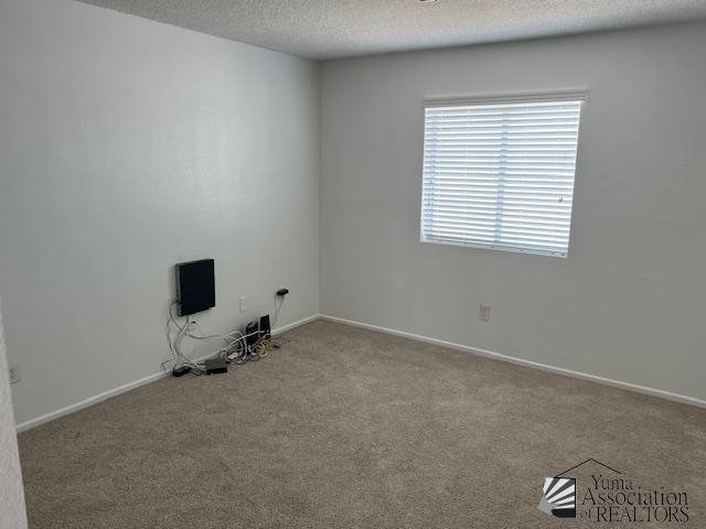 carpeted empty room with baseboards and a textured ceiling