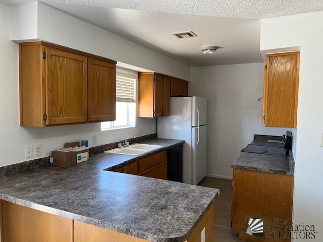 kitchen with black dishwasher, visible vents, dark countertops, a peninsula, and a sink