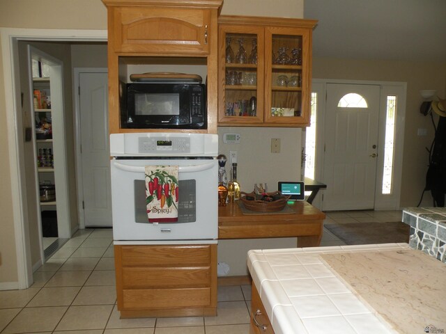 10224 S Fairway Ln, Yuma, AZ 85367 - kitchen featuring oven, tile counters, black microwave, light tile patterned floors, and glass insert cabinets