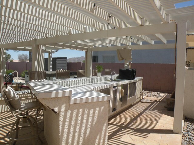 10224 S Fairway Ln, Yuma, AZ 85367 - view of patio / terrace featuring fence, an outdoor kitchen, a mountain view, and a pergola