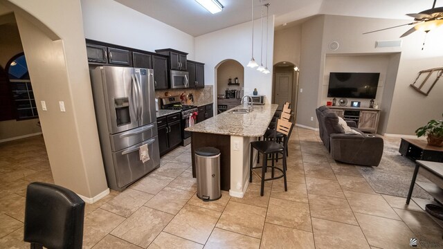 kitchen featuring ceiling fan, a kitchen bar, arched walkways, open floor plan, and stainless steel appliances