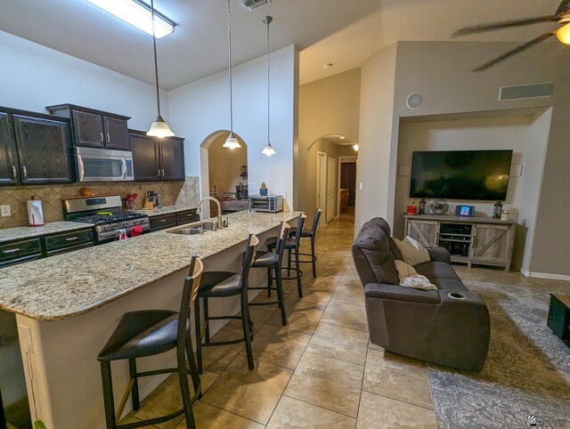 kitchen with appliances with stainless steel finishes, arched walkways, a sink, open floor plan, and a breakfast bar