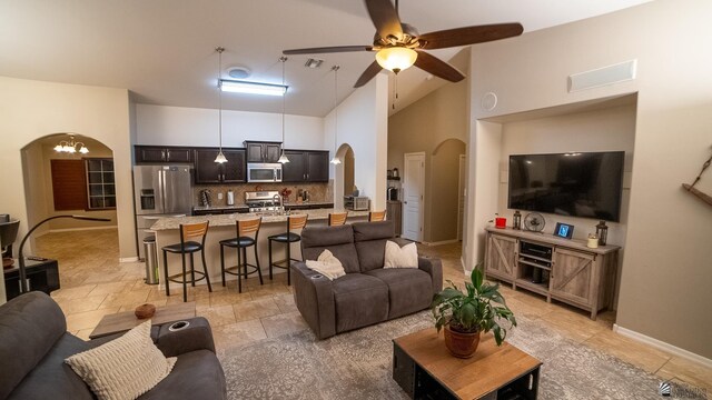 living area with baseboards, arched walkways, ceiling fan with notable chandelier, and high vaulted ceiling