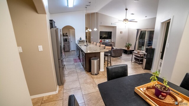 kitchen featuring freestanding refrigerator, open floor plan, a kitchen breakfast bar, ceiling fan, and arched walkways