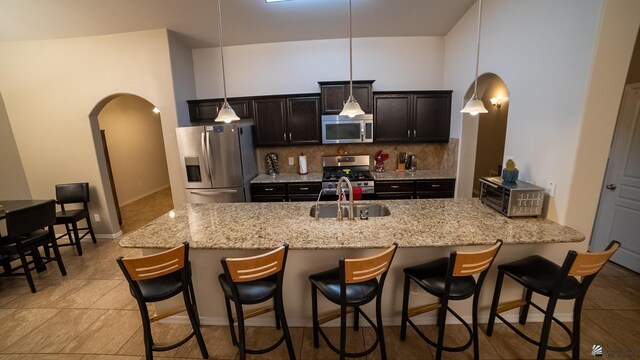 kitchen with decorative backsplash, a breakfast bar, arched walkways, a sink, and stainless steel appliances