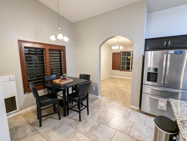 dining area featuring arched walkways, light tile patterned floors, baseboards, high vaulted ceiling, and an inviting chandelier