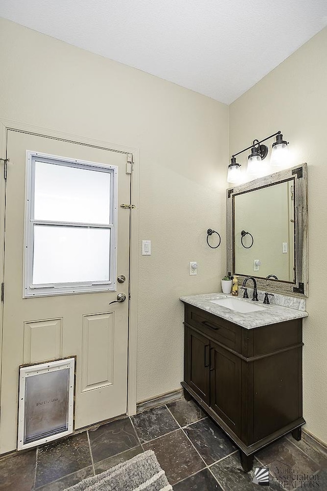bathroom with vanity, baseboards, and stone tile flooring