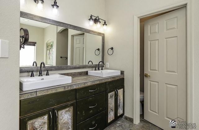 bathroom with a sink, toilet, and double vanity