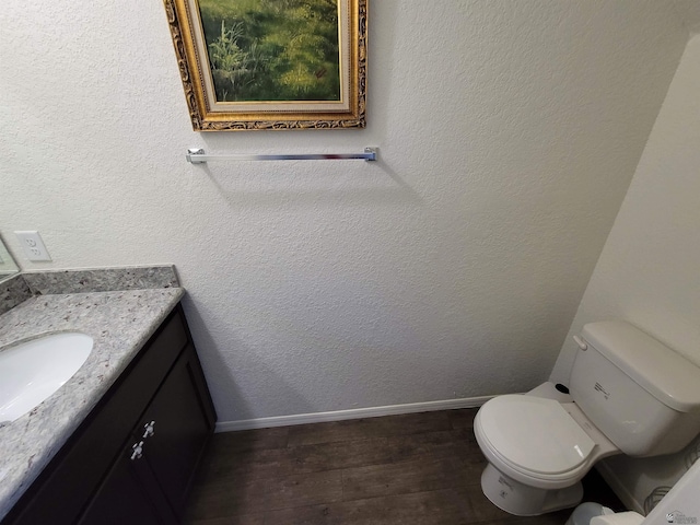 half bathroom with vanity, baseboards, toilet, and wood finished floors