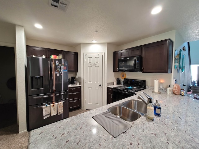 kitchen with dark brown cabinetry, visible vents, light stone countertops, a sink, and black appliances