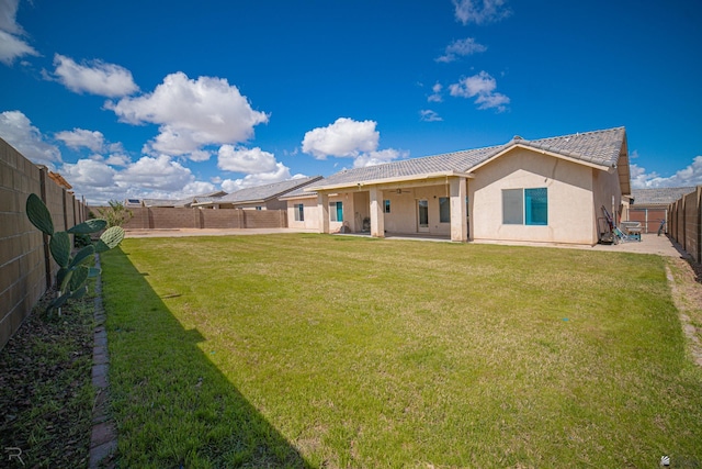 back of property with a lawn, ceiling fan, a fenced backyard, and a patio area