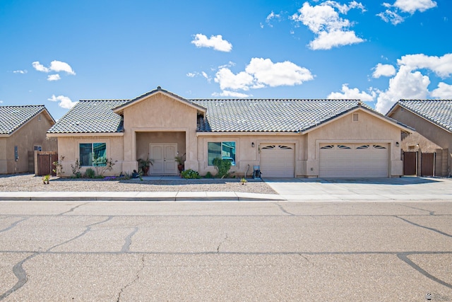 view of front of house with a tiled roof, a garage, fence, concrete driveway, and stucco siding