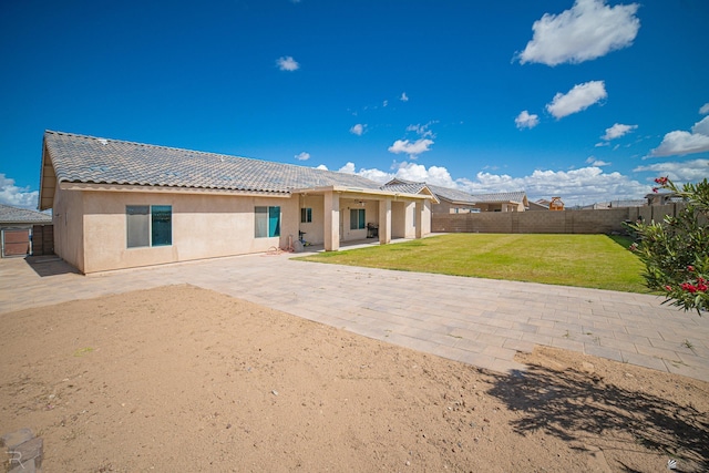 back of property with a tile roof, stucco siding, a fenced backyard, a patio area, and a yard