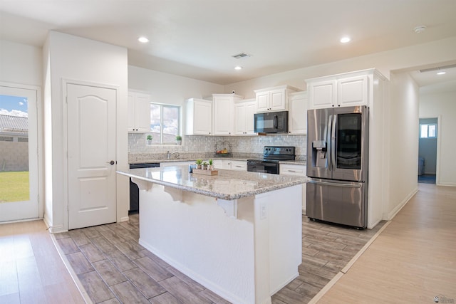 kitchen featuring a kitchen island, a kitchen breakfast bar, black appliances, and light wood-style floors