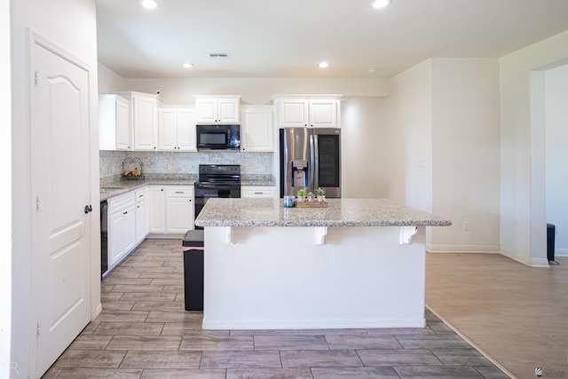kitchen featuring visible vents, a kitchen island, black appliances, and light wood-type flooring