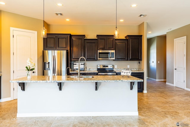 14817 E 47th Dr, Yuma, AZ 85367 - kitchen featuring appliances with stainless steel finishes, a breakfast bar area, dark brown cabinets, an island with sink, and light stone countertops