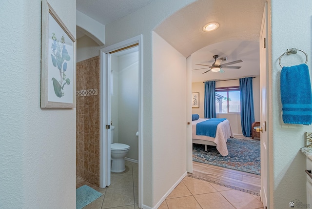 bathroom with a textured wall, toilet, ceiling fan, tile patterned floors, and ensuite bath