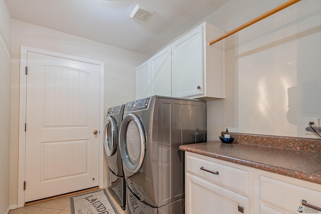 washroom with visible vents, cabinet space, light tile patterned floors, and washing machine and clothes dryer