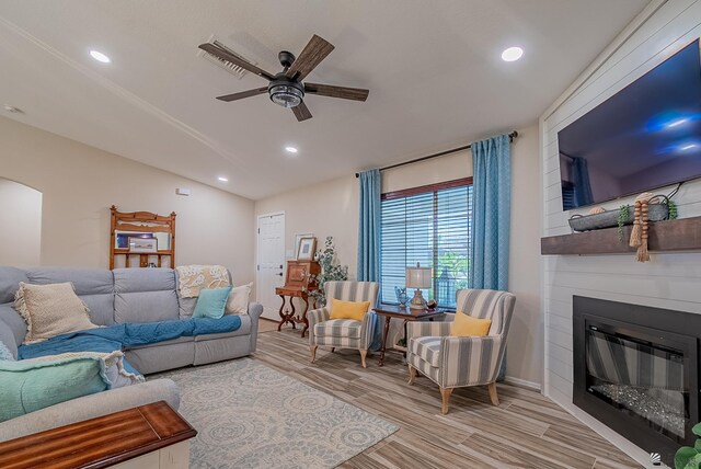 living area with wood finished floors, recessed lighting, a large fireplace, a ceiling fan, and vaulted ceiling
