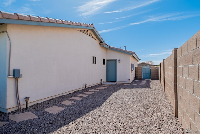 rear view of property with fence, a gate, stucco siding, and a tiled roof