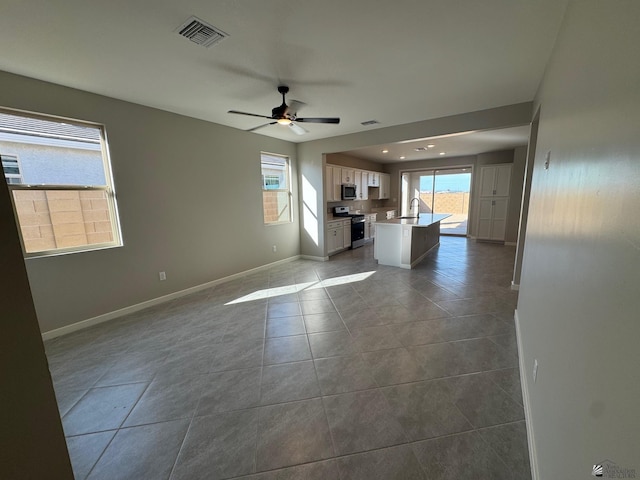 unfurnished living room with a sink, a ceiling fan, baseboards, dark tile patterned flooring, and visible vents