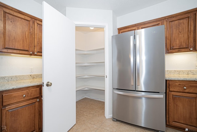11250 E 25th Pl, Yuma, AZ 85367 - kitchen with freestanding refrigerator, brown cabinets, light stone counters, and light tile patterned floors