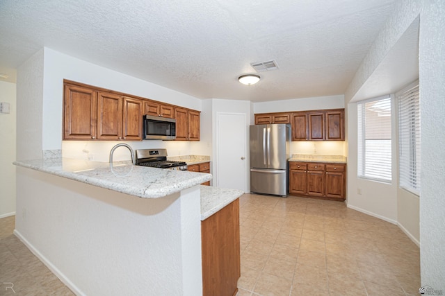 11250 E 25th Pl, Yuma, AZ 85367 - kitchen featuring stainless steel appliances, brown cabinets, a peninsula, light stone counters, and a textured ceiling
