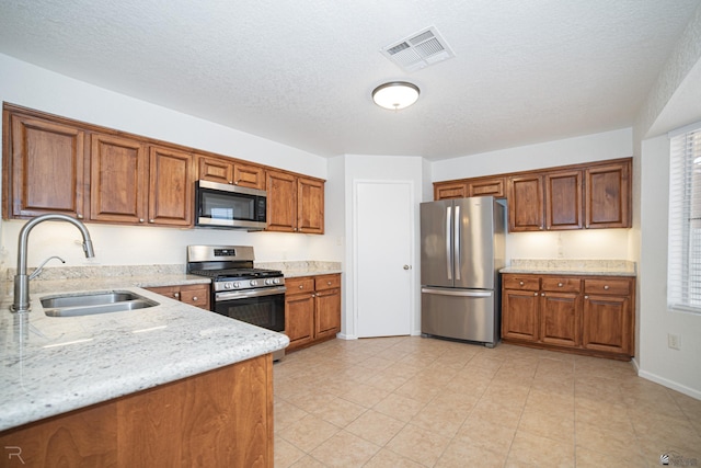 11250 E 25th Pl, Yuma, AZ 85367 - kitchen featuring appliances with stainless steel finishes, a sink, brown cabinetry, light stone counters, and a textured ceiling