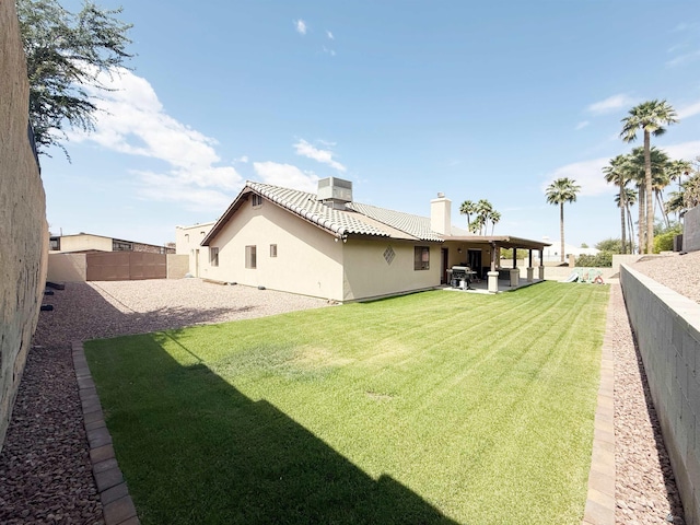 rear view of house featuring a yard, a patio, stucco siding, a fenced backyard, and a chimney