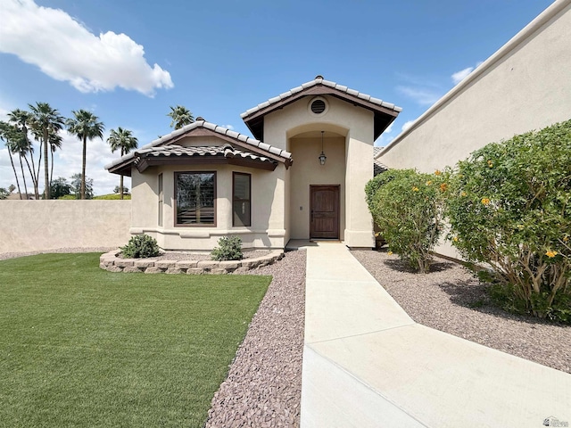 mediterranean / spanish-style house with fence, stucco siding, a front lawn, and a tiled roof