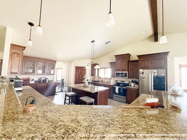 kitchen with lofted ceiling with beams, a breakfast bar, a center island, light stone countertops, and appliances with stainless steel finishes