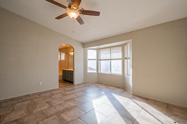 empty room with arched walkways, ceiling fan, and baseboards